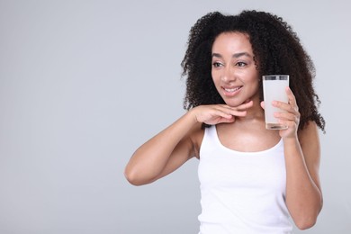 Photo of Beautiful Brazilian woman with glass of collagen water on gray background. Space for text