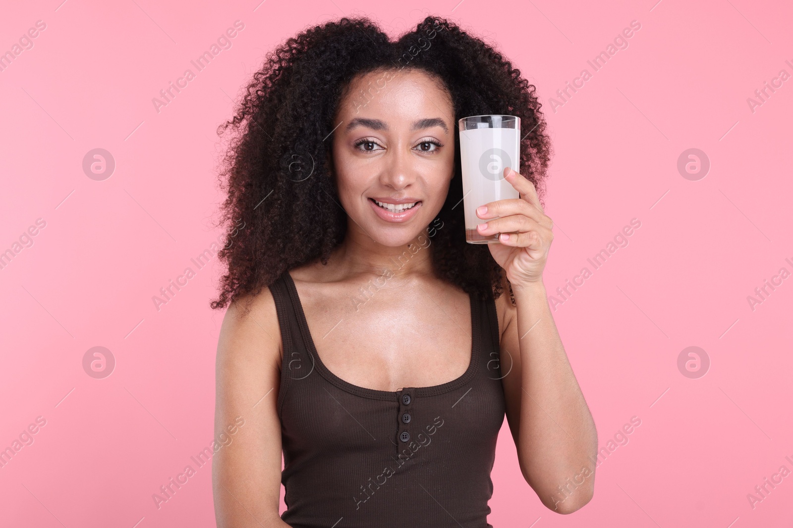 Beautiful Brazilian woman with glass of collagen water on pink background Photo of Beautiful Brazilian woman with glass of collagen water on pink background