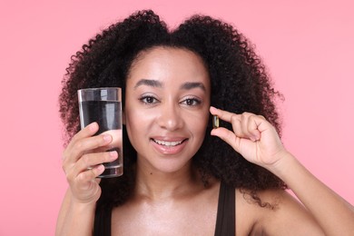 Photo of Beautiful Brazilian woman with glass of water and collagen pill on pink background