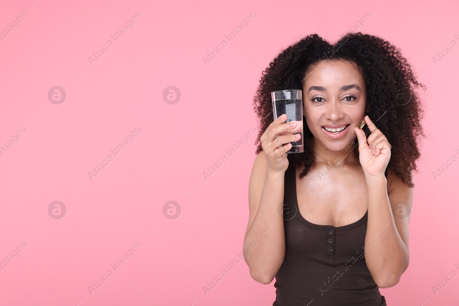 Beautiful Brazilian woman with glass of water and collagen pill on pink background. Space for text Photo of Beautiful Brazilian woman with glass of water and collagen pill on pink background. Space for text
