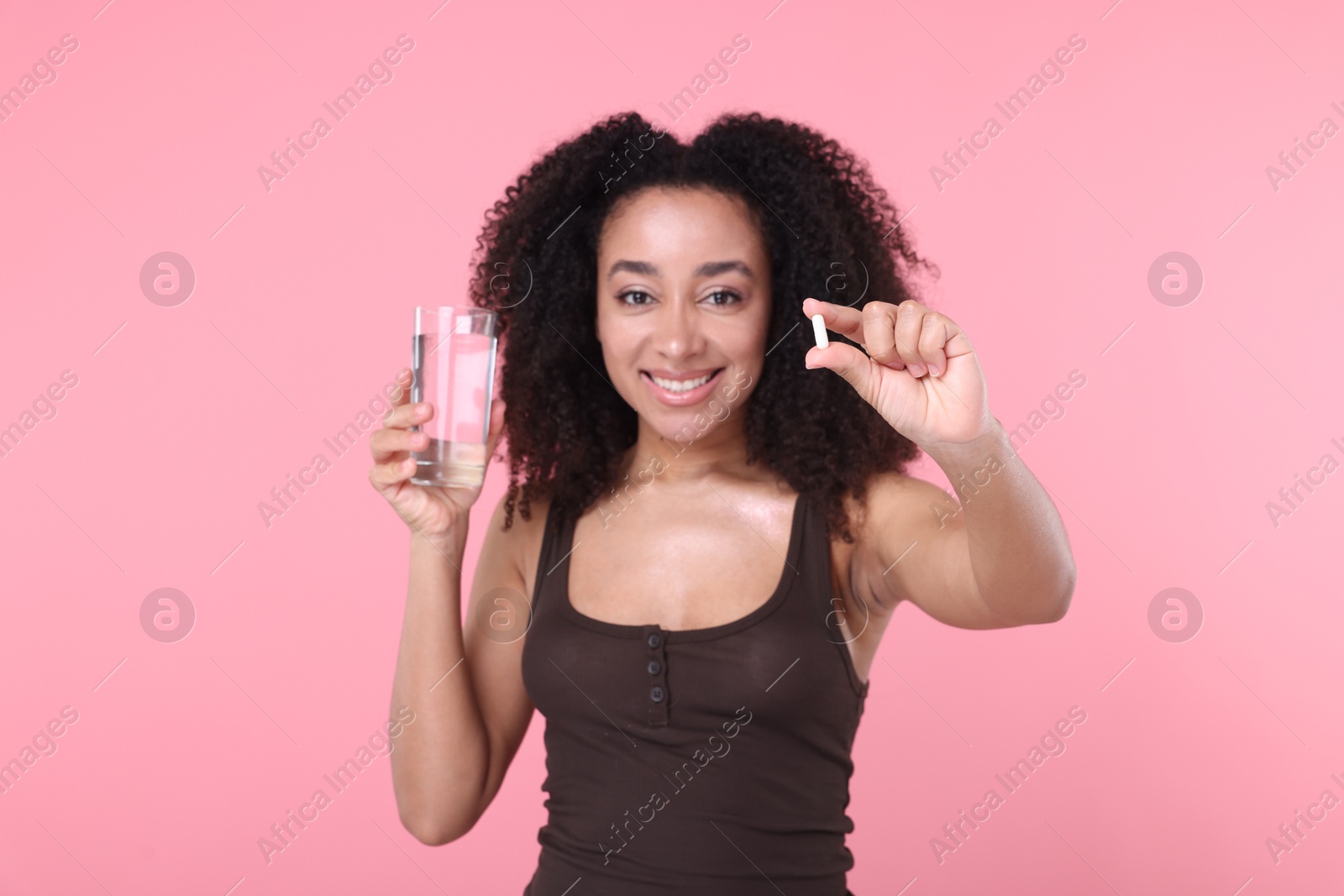 Beautiful Brazilian woman with glass of water and collagen pill on pink background Photo of Beautiful Brazilian woman with glass of water and collagen pill on pink background