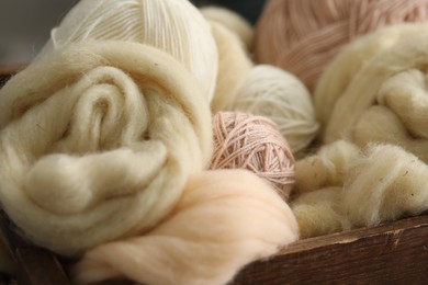 Photo of Soft felting wool and knitting yarn in wooden basket, closeup