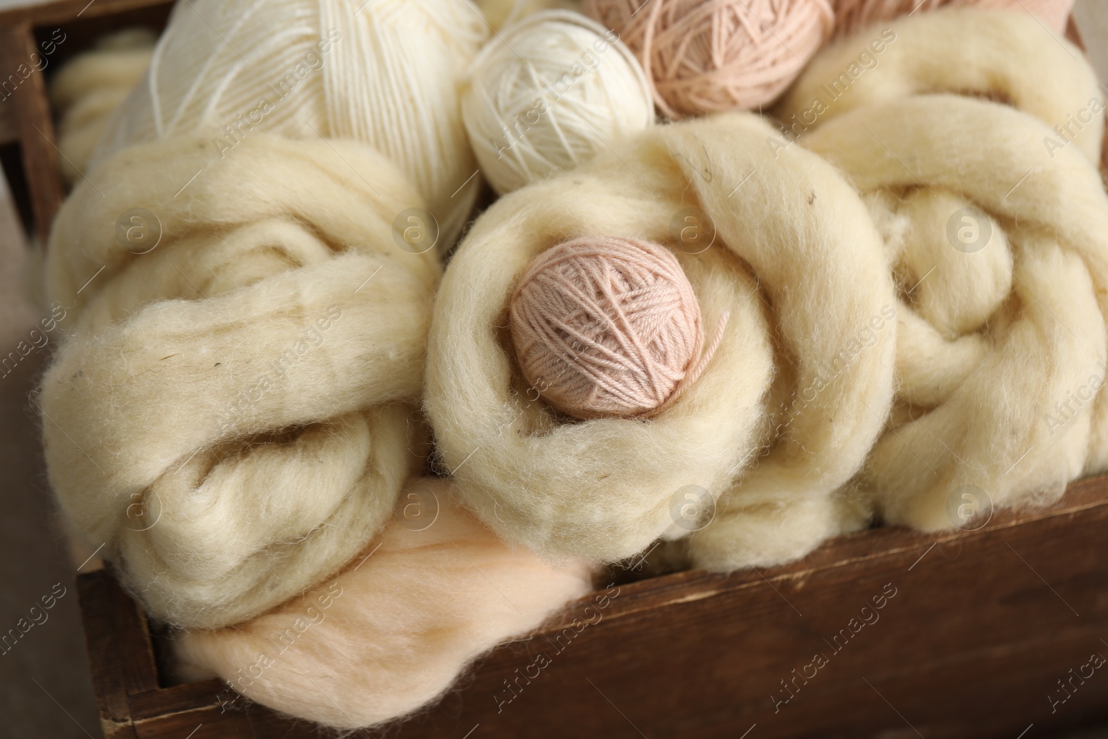 Photo of Soft felting wool and knitting yarn in wooden basket, closeup
