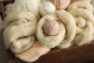 Photo of Soft felting wool and knitting yarn in wooden basket, closeup