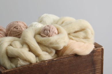Photo of Soft felting wool and knitting yarn in wooden basket on grey background, closeup