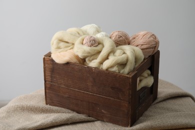 Photo of Soft felting wool and knitting yarn in wooden basket on grey background