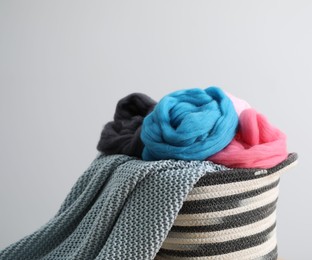Photo of Soft felting wool and knitting yarn in basket against light grey background, closeup