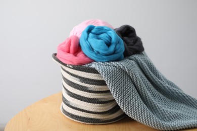 Photo of Soft felting wool and knitting yarn in basket on wooden table against light grey background