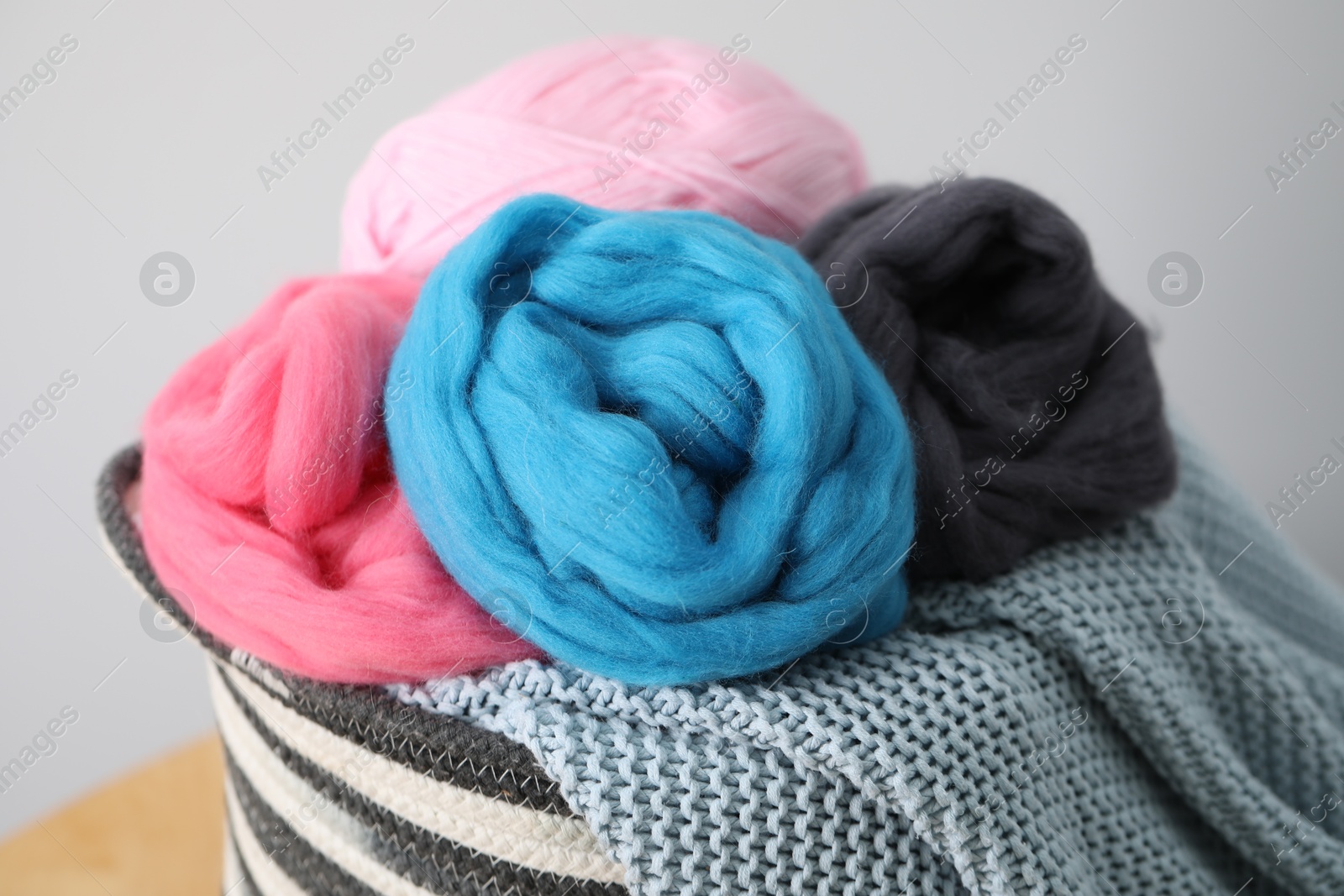Soft felting wool and knitting yarn in basket on wooden table against light grey background, closeup Photo of Soft felting wool and knitting yarn in basket on wooden table against light grey background, closeup