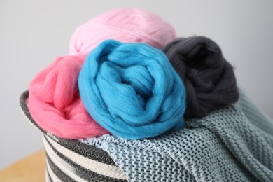 Photo of Soft felting wool and knitting yarn in basket on wooden table against light grey background, closeup