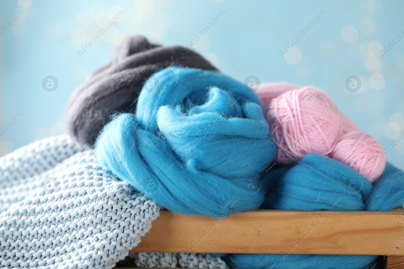 Soft felting wool and knitting yarn in wooden crate against light blue background with blurred lights, closeup Photo of Soft felting wool and knitting yarn in wooden crate against light blue background with blurred lights, closeup