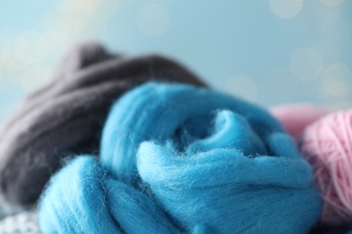 Photo of Soft felting wool and knitting yarn against light blue background with blurred lights, closeup
