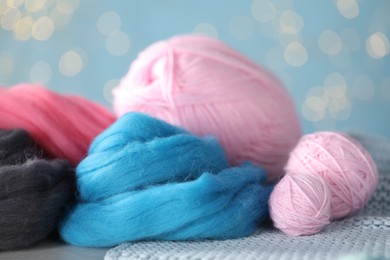 Photo of Soft felting wool and knitting yarn on white wooden table against light blue background with blurred lights, closeup