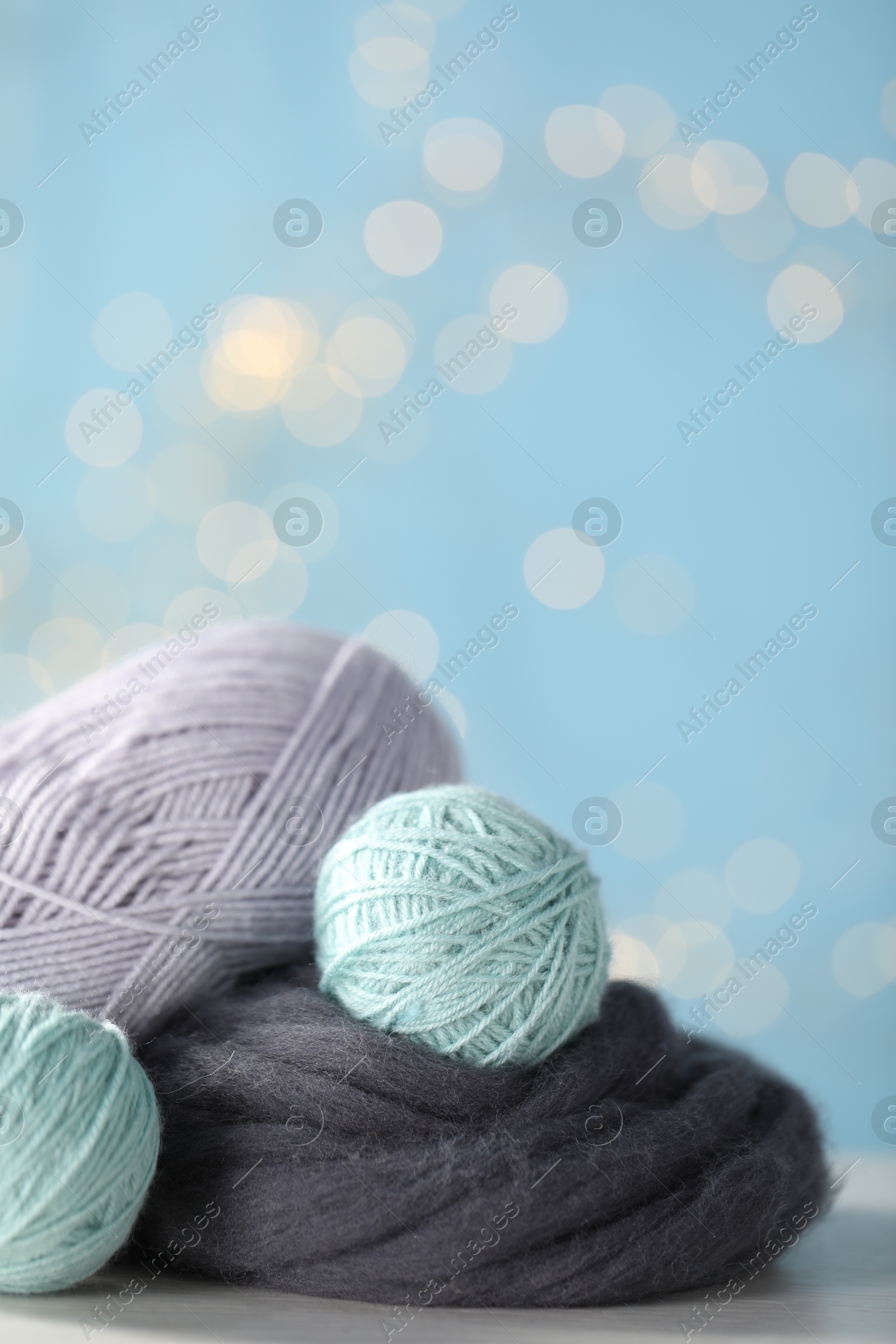 Photo of Soft felting wool and knitting yarn on white wooden table against light blue background with blurred lights, closeup