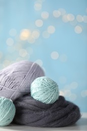 Photo of Soft felting wool and knitting yarn on white wooden table against light blue background with blurred lights, closeup