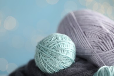 Photo of Soft felting wool and knitting yarn against light blue background with blurred lights, closeup