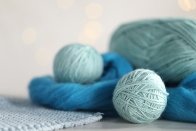 Photo of Soft felting wool and knitting yarn on white wooden table against blurred lights, closeup