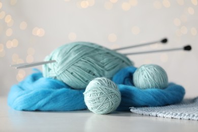 Photo of Soft felting wool and knitting yarn on white wooden table against blurred lights, closeup