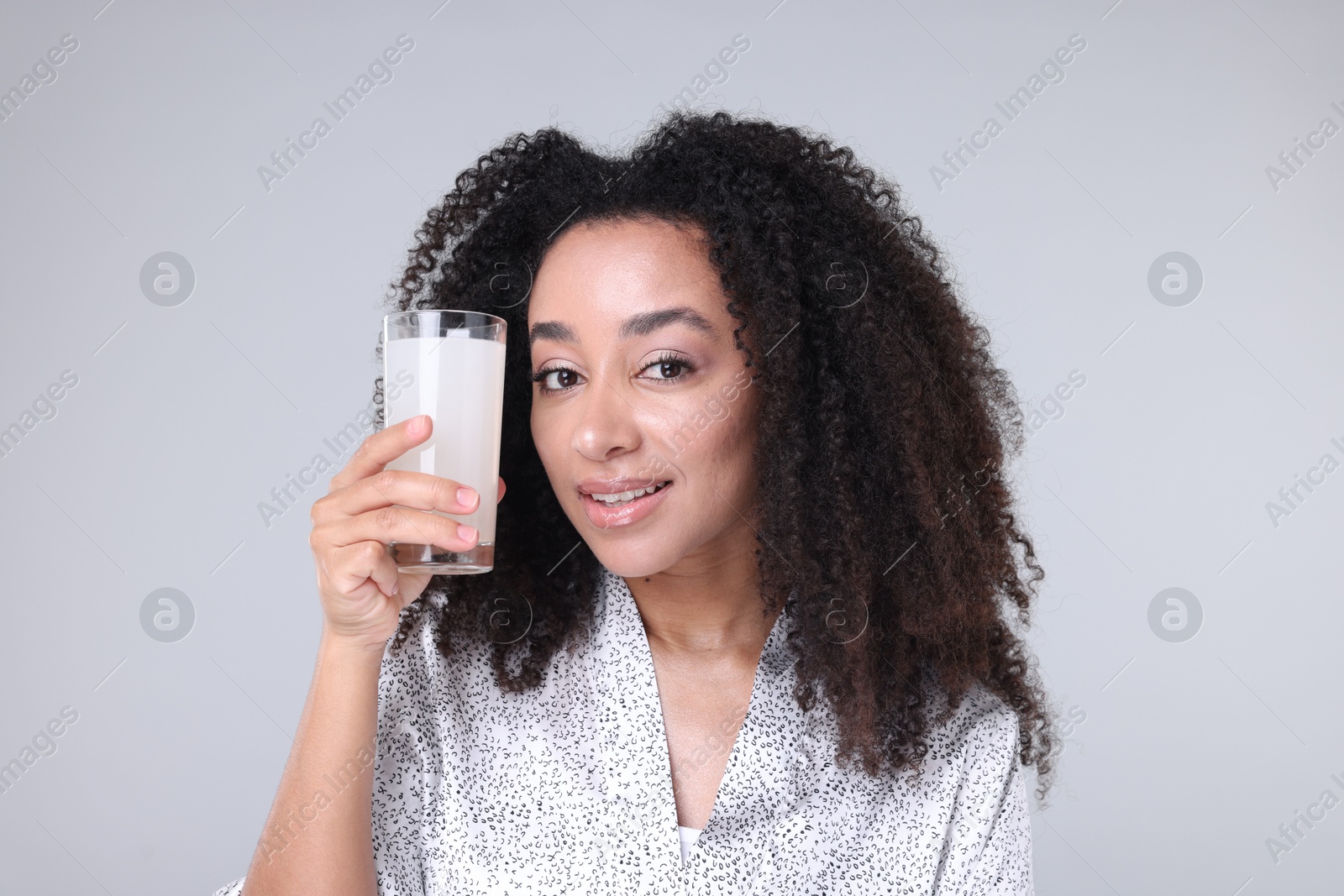 Beautiful Brazilian woman with glass of collagen water on gray background Photo of Beautiful Brazilian woman with glass of collagen water on gray background