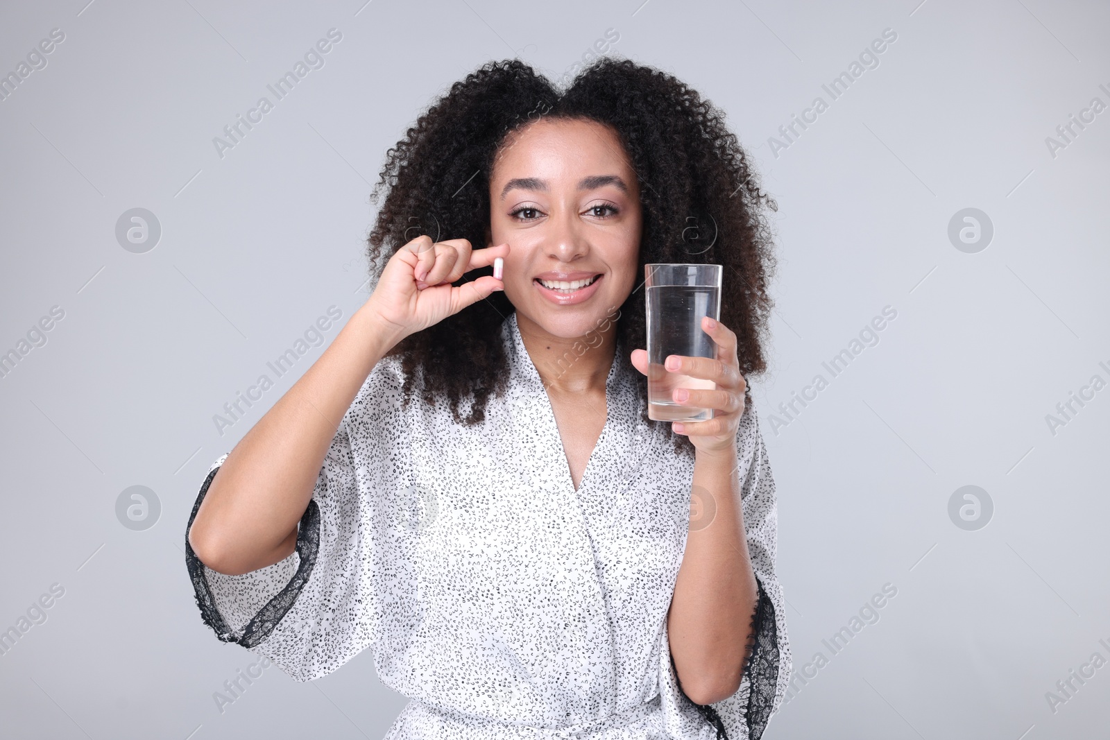 Beautiful Brazilian woman with glass of water and collagen pill on gray background Photo of Beautiful Brazilian woman with glass of water and collagen pill on gray background