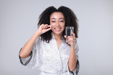Photo of Beautiful Brazilian woman with glass of water and collagen pill on gray background