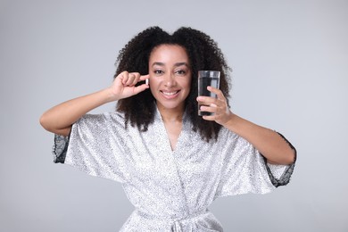 Photo of Beautiful Brazilian woman with glass of water and collagen pill on gray background