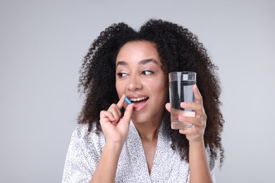 Photo of Beautiful Brazilian woman with glass of water taking collagen pill on gray background