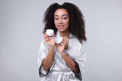 Photo of Beautiful Brazilian woman with jar of collagen cream on gray background