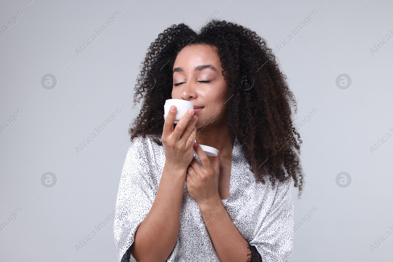 Beautiful Brazilian woman with jar of collagen cream on gray background Photo of Beautiful Brazilian woman with jar of collagen cream on gray background