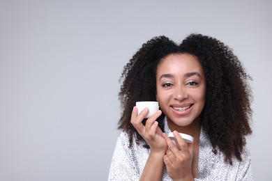 Photo of Beautiful Brazilian woman with jar of collagen cream on gray background. Space for text