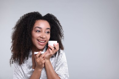 Photo of Beautiful Brazilian woman with jar of collagen cream on gray background. Space for text