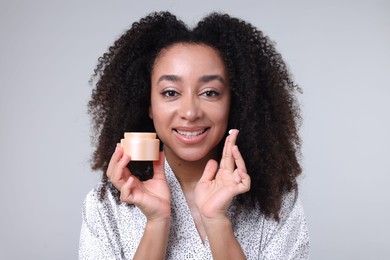 Photo of Beautiful Brazilian woman with jar of collagen cream on gray background
