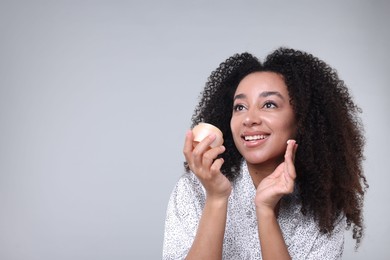 Photo of Beautiful Brazilian woman with jar of collagen cream on gray background. Space for text