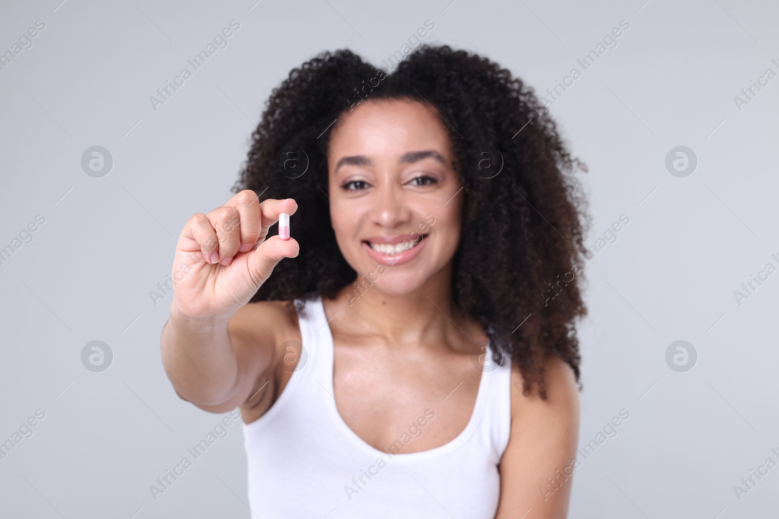 Beautiful Brazilian woman with collagen pill on gray background, selective focus Photo of Beautiful Brazilian woman with collagen pill on gray background, selective focus