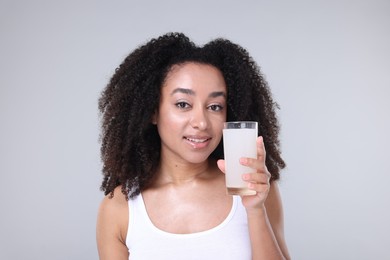 Photo of Beautiful Brazilian woman with glass of collagen water on gray background