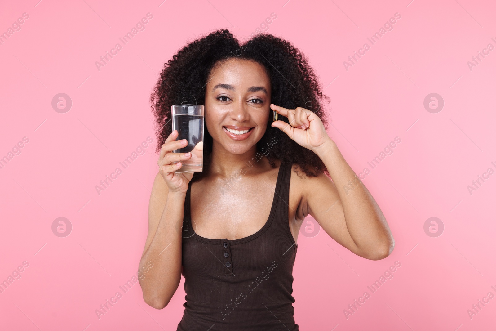 Beautiful Brazilian woman with glass of water and collagen pill on pink background Photo of Beautiful Brazilian woman with glass of water and collagen pill on pink background