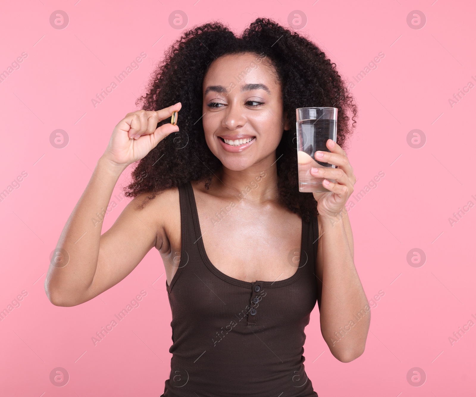 Beautiful Brazilian woman with glass of water and collagen pill on pink background Photo of Beautiful Brazilian woman with glass of water and collagen pill on pink background