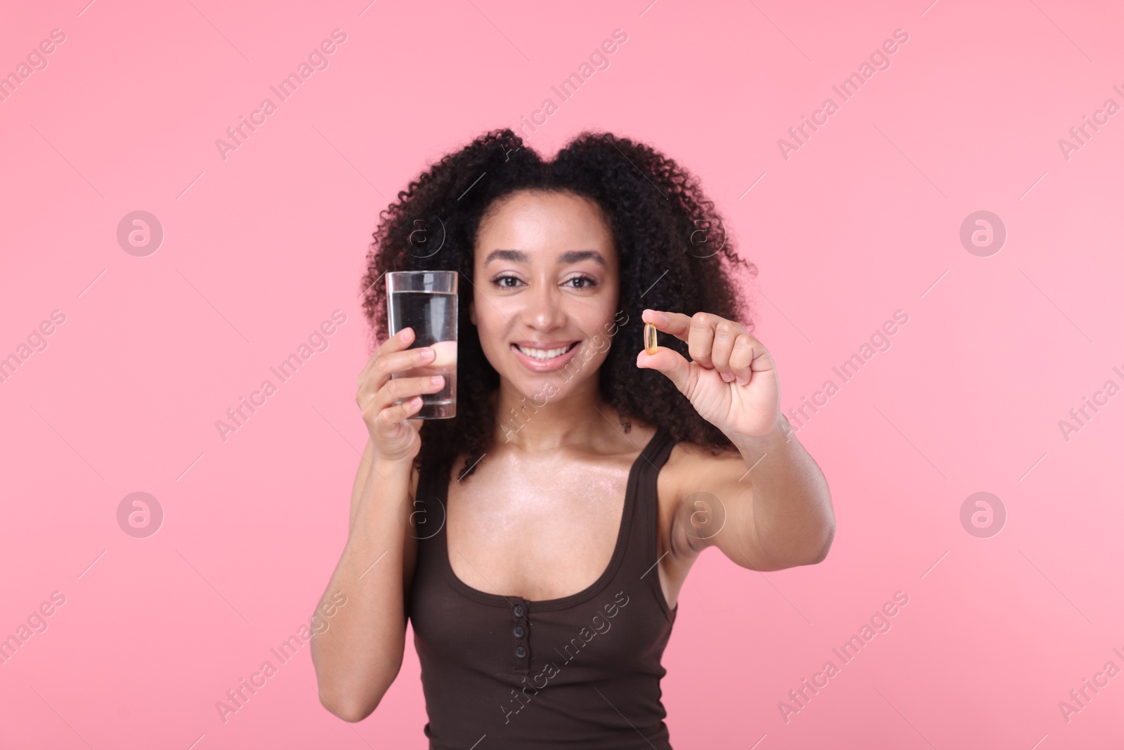 Beautiful Brazilian woman with glass of water and collagen pill on pink background Photo of Beautiful Brazilian woman with glass of water and collagen pill on pink background