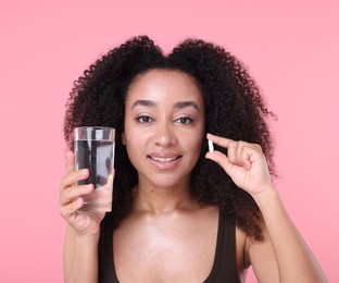 Photo of Beautiful Brazilian woman with glass of water and collagen pill on pink background