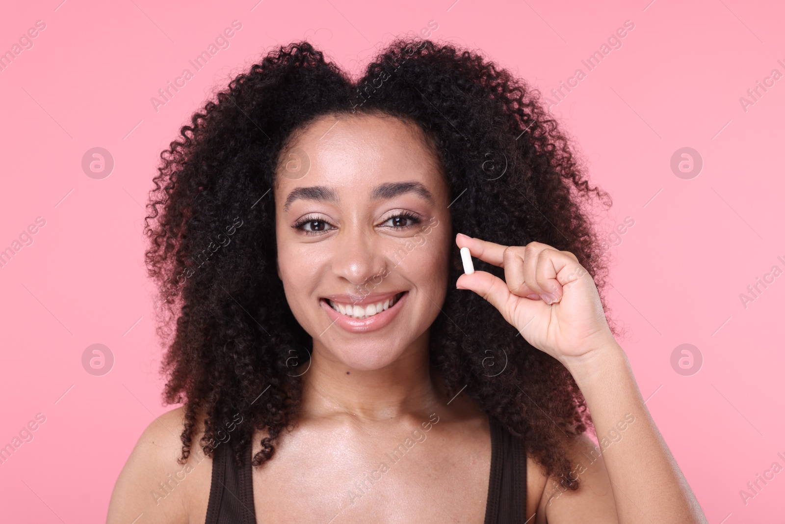 Beautiful Brazilian woman with collagen pill on pink background Photo of Beautiful Brazilian woman with collagen pill on pink background