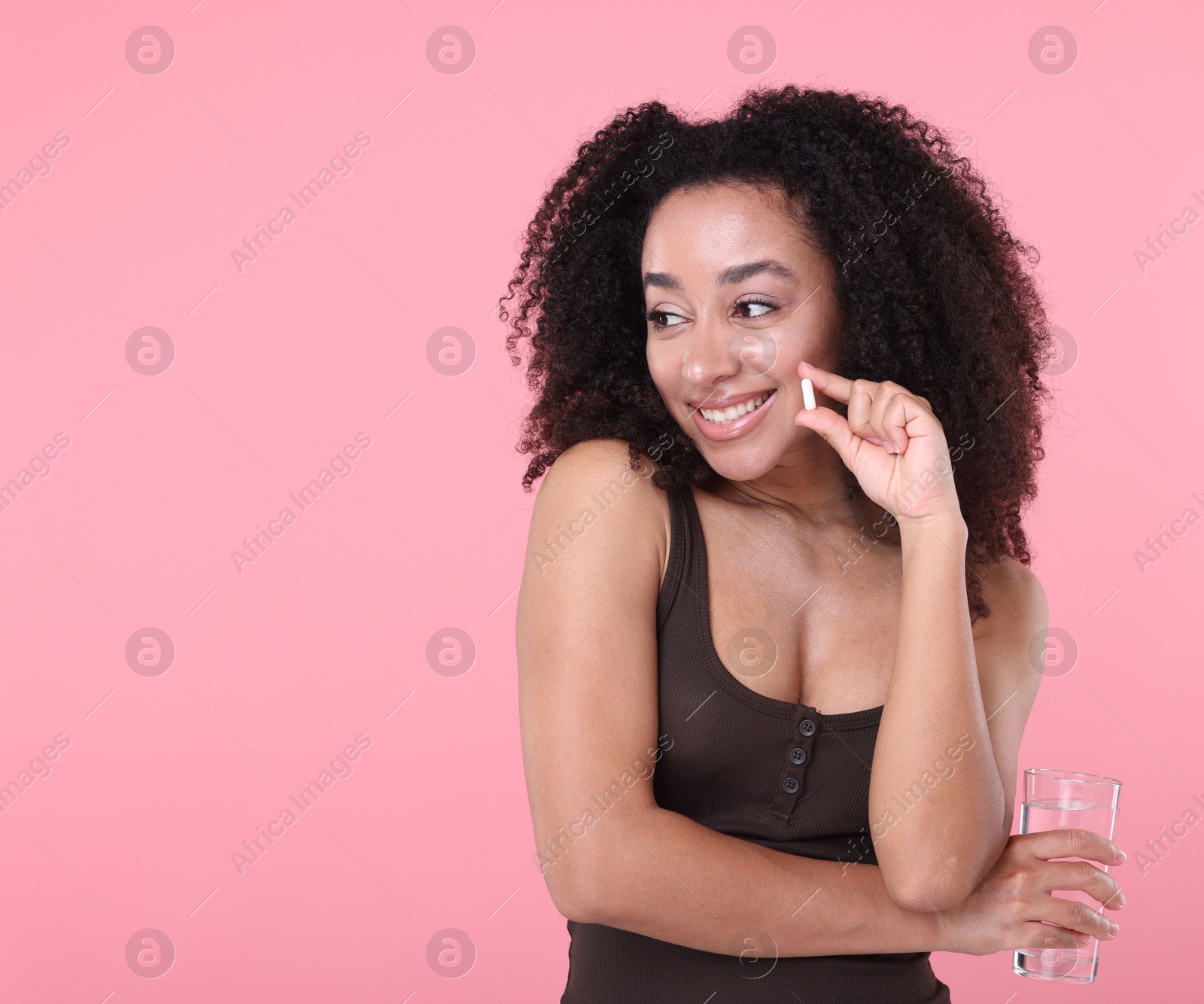 Beautiful Brazilian woman with glass of water and collagen pill on pink background. Space for text Photo of Beautiful Brazilian woman with glass of water and collagen pill on pink background. Space for text