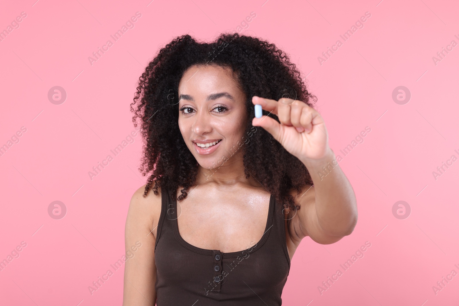 Beautiful Brazilian woman with collagen pill on pink background Photo of Beautiful Brazilian woman with collagen pill on pink background