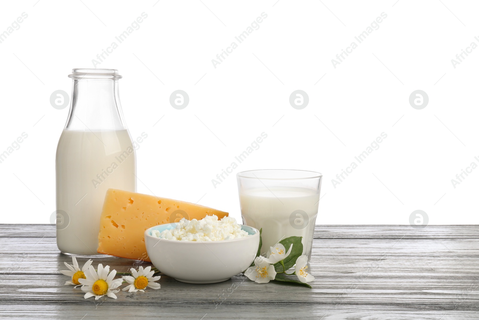 Different fresh dairy products and flowers on grey wooden table against white background Photo of Different fresh dairy products and flowers on grey wooden table against white background
