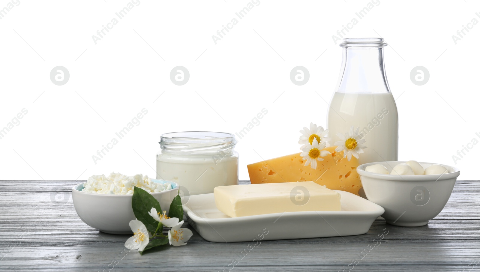 Different fresh dairy products and flowers on grey wooden table against white background Photo of Different fresh dairy products and flowers on grey wooden table against white background