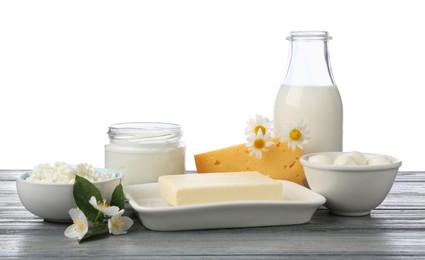 Photo of Different fresh dairy products and flowers on grey wooden table against white background
