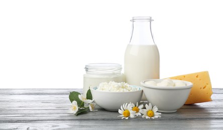 Photo of Different fresh dairy products and flowers on grey wooden table against white background