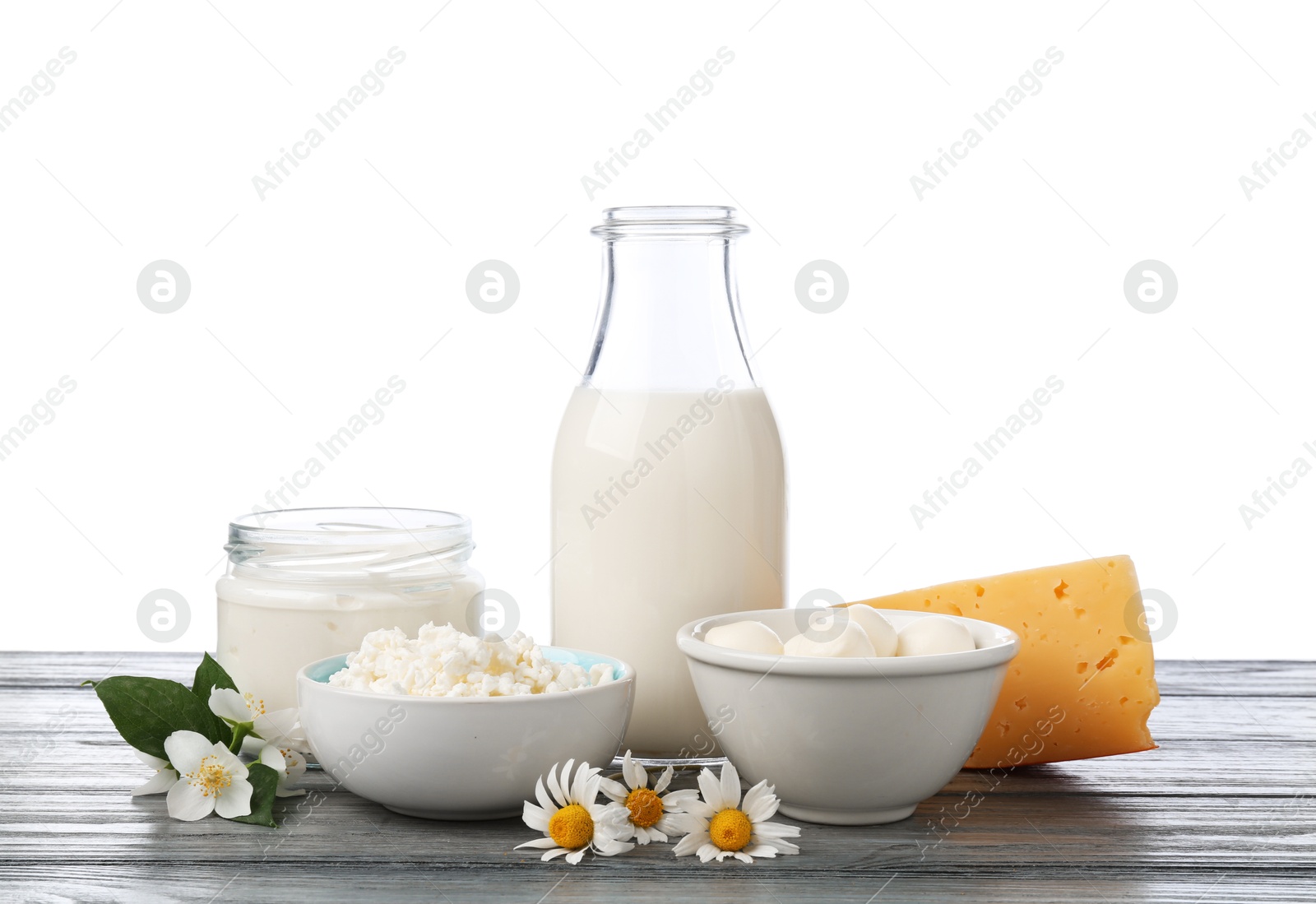 Different fresh dairy products and flowers on grey wooden table against white background Photo of Different fresh dairy products and flowers on grey wooden table against white background