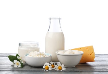 Photo of Different fresh dairy products and flowers on grey wooden table against white background