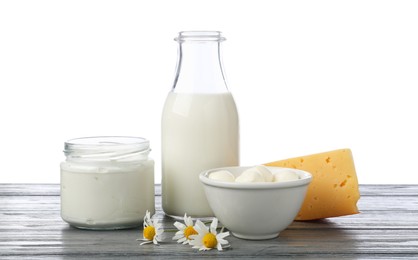 Photo of Different fresh dairy products and chamomile flowers on grey wooden table against white background