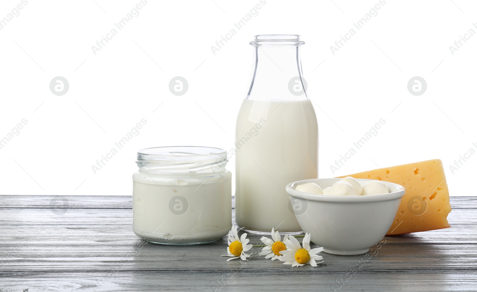 Photo of Different fresh dairy products and chamomile flowers on grey wooden table against white background